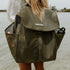 An image of a woman with long blonde hair standing at the water’s edge, wearing the Sande Kids™ Beach Hauler mesh backpack in Pandanus, a dark olive green. The backpack features side pockets, a flap that clips up, and displays a silicone Sande Kids™ logo in white.