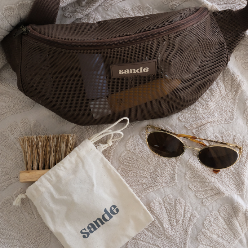 Sande mesh Essentials Crossbody bag in Espresso with Sand Brush - Mini, styled on a neutral towel with sunglasses and cotton storage pouch.