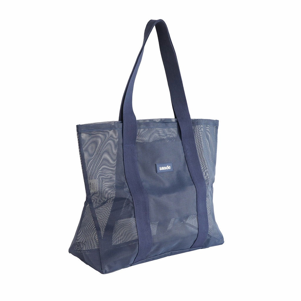 Sande Kids Beach Hauler - large mesh beach bag in Deep Sea Navy, displayed in a studio setting at a 45° angle. This view highlights the mesh detail, thick cotton straps, durable construction, and the silicone label with the Sande logo. Set against a white background.
