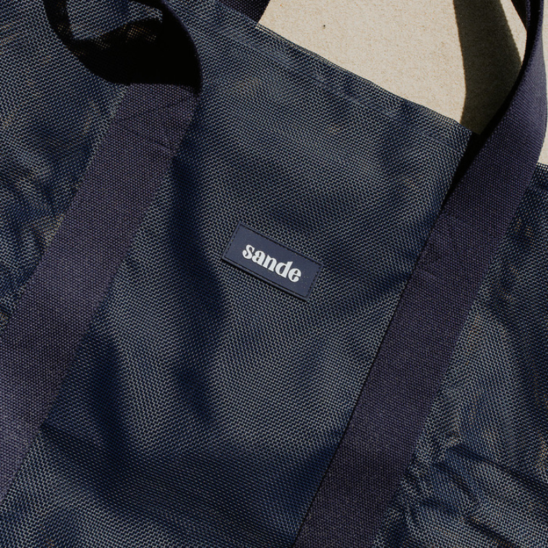 Close-up of the high-quality features of the Sande Kids Beach Hauler mesh beach bag in Deep Sea Navy. Highlights the durable PVC mesh fabric, thick cotton straps, and silicone Sande logo.
