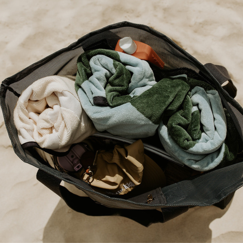 Top view of the Sande Kids Beach Hauler - Mini, a large mesh beach bag in Deep Sea Navy resting on the sand. This image highlights the large capacity of the mesh beach bag, showcasing its ability to fit beach towels, hats, sunscreen, snacks, water bottles, and valuables—making it the perfect beach bag for all your essentials.