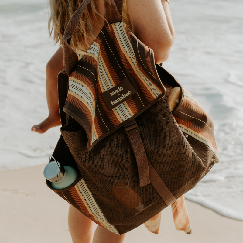 A woman wears the Banabae x Sande backpack slung over one shoulder, with the ocean in the background.