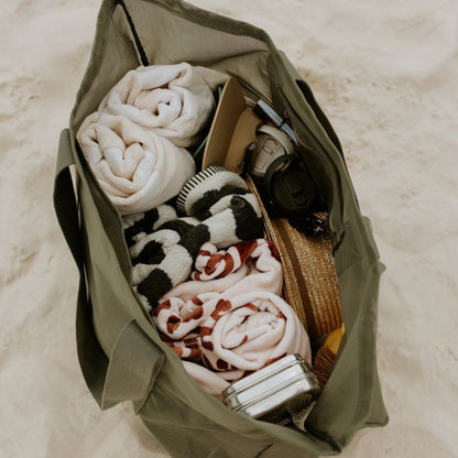 Image to demonstrate what fits in to the Sande Kids Beach Hauler - oversized mesh beach bag. Colour is Pandanus green. Packed inside are beach towels, beach toys, sand brush, sunscreen, water bottles.