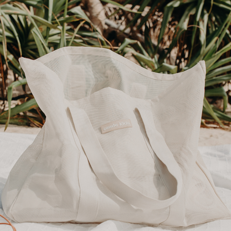 Oversized Sande Kids Beach Hauler™ mesh beach bag with pandanus trees in the background, highlighting its large capacity and family-friendly design.