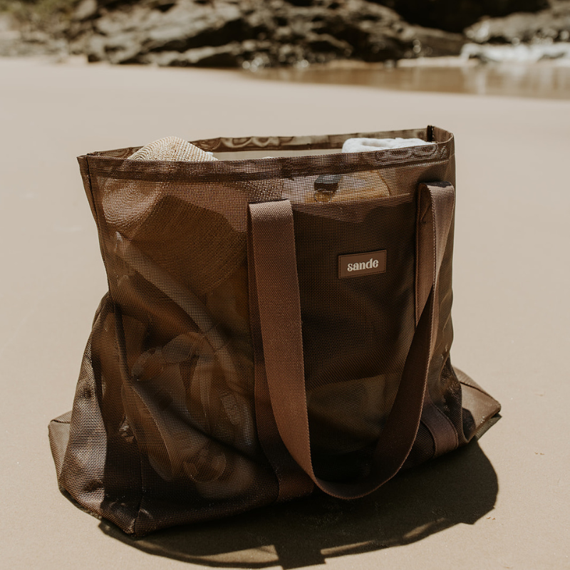 The Sande oversized Beach Hauler mesh beach bag in Espresso brown sitting full to the brim on the beach.