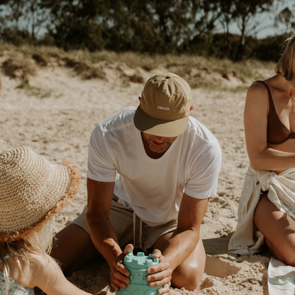 A lifestyle image of dad wearing the beige waterproof Sande™ cap while building sandcastles on the beach with his family.