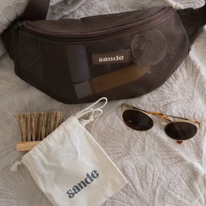 Sande mesh Essentials Crossbody bag in Espresso with Sand Brush - Mini, styled on a neutral towel with sunglasses and cotton storage pouch.