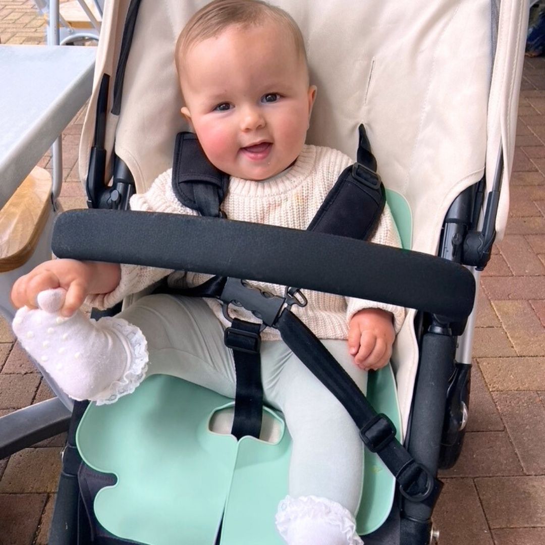 A baby girl sitting in her Bugaboo pram with a Seafoam Green Sande Kids™ silicone car seat and pram liner.