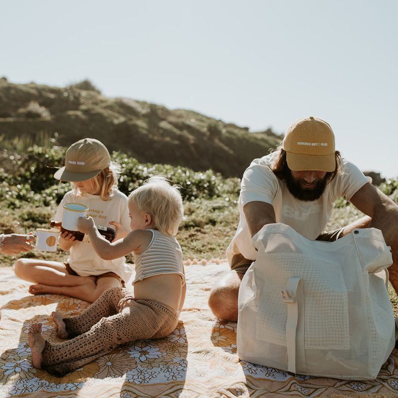 Dad and kids enjoying a picnic at Cabarita Headland, with dad using the Sande Kids Beach Hauler mesh backpack in Sand colour.